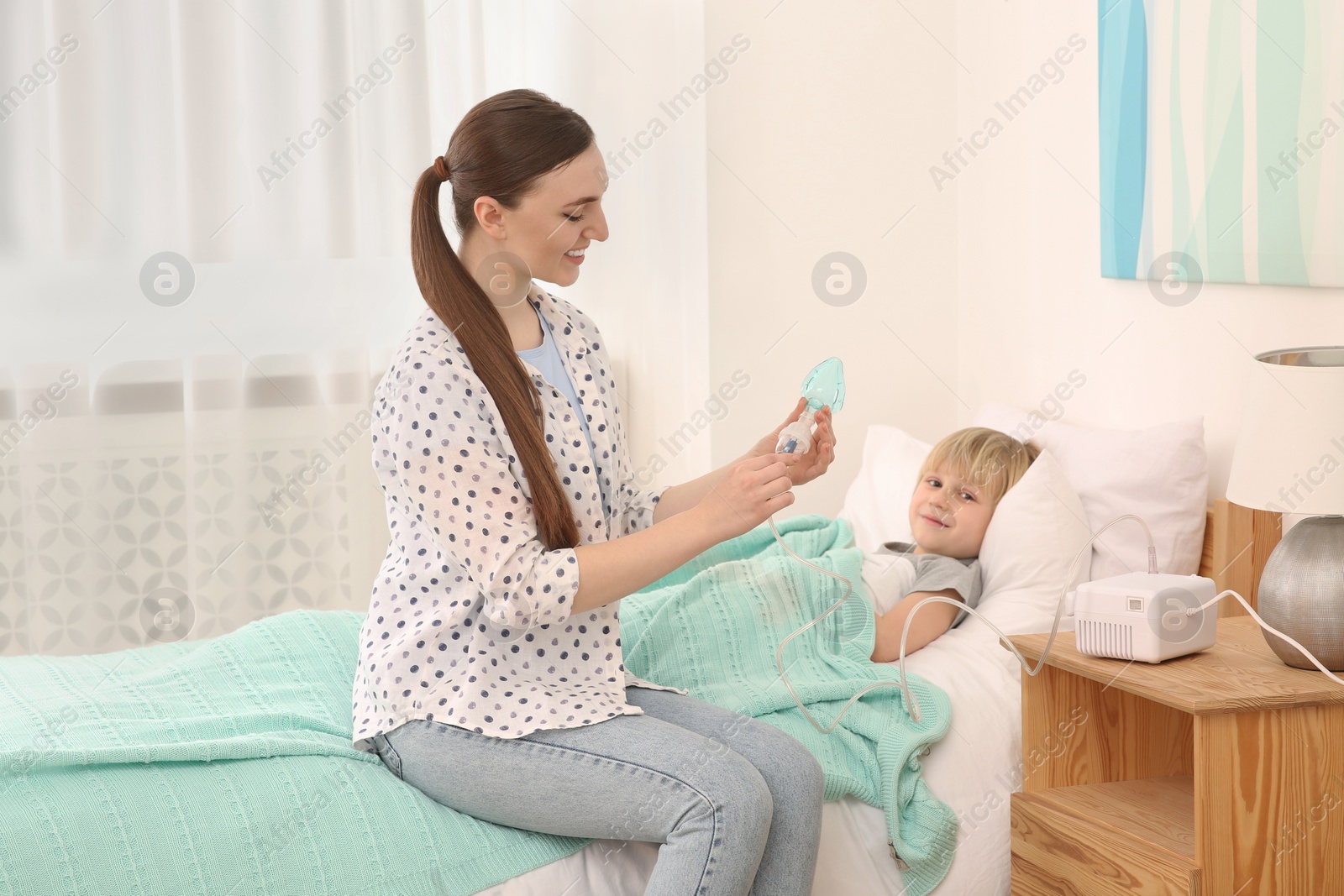 Photo of Mother holding nebulizer for inhalation and her son lying on bed at home