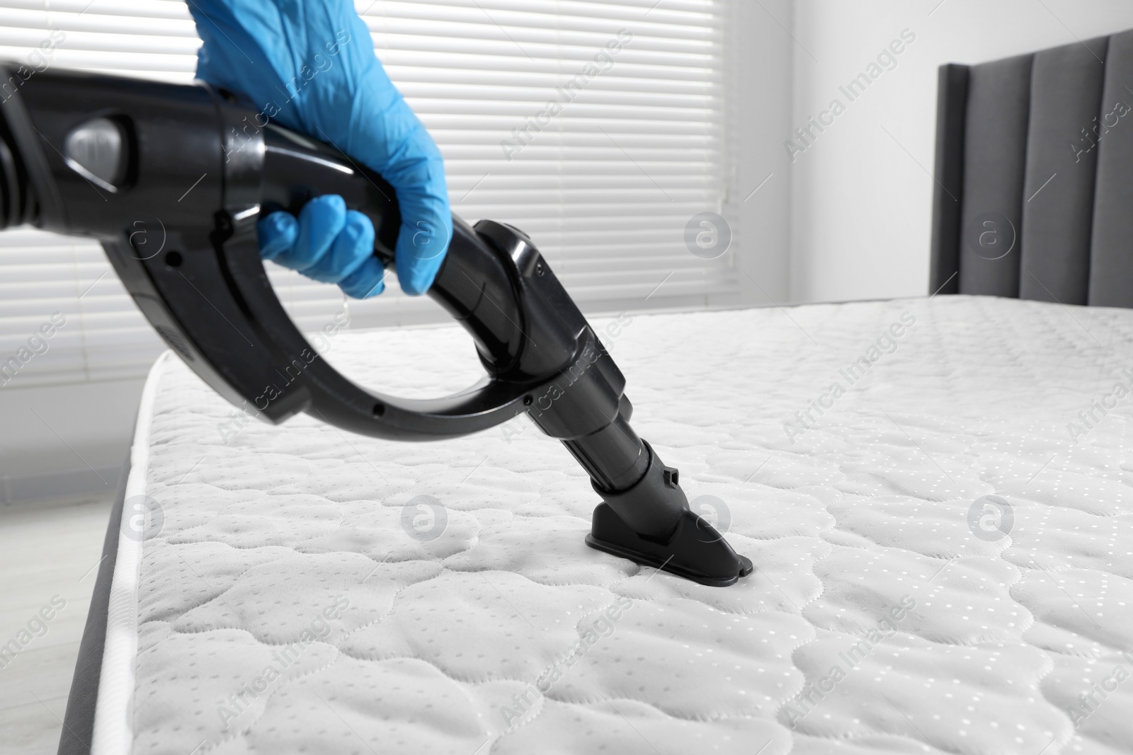 Photo of Person disinfecting mattress with vacuum cleaner indoors, closeup