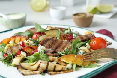 Delicious salad with beef tongue, grilled vegetables, peach, blue cheese and fork served on table, closeup