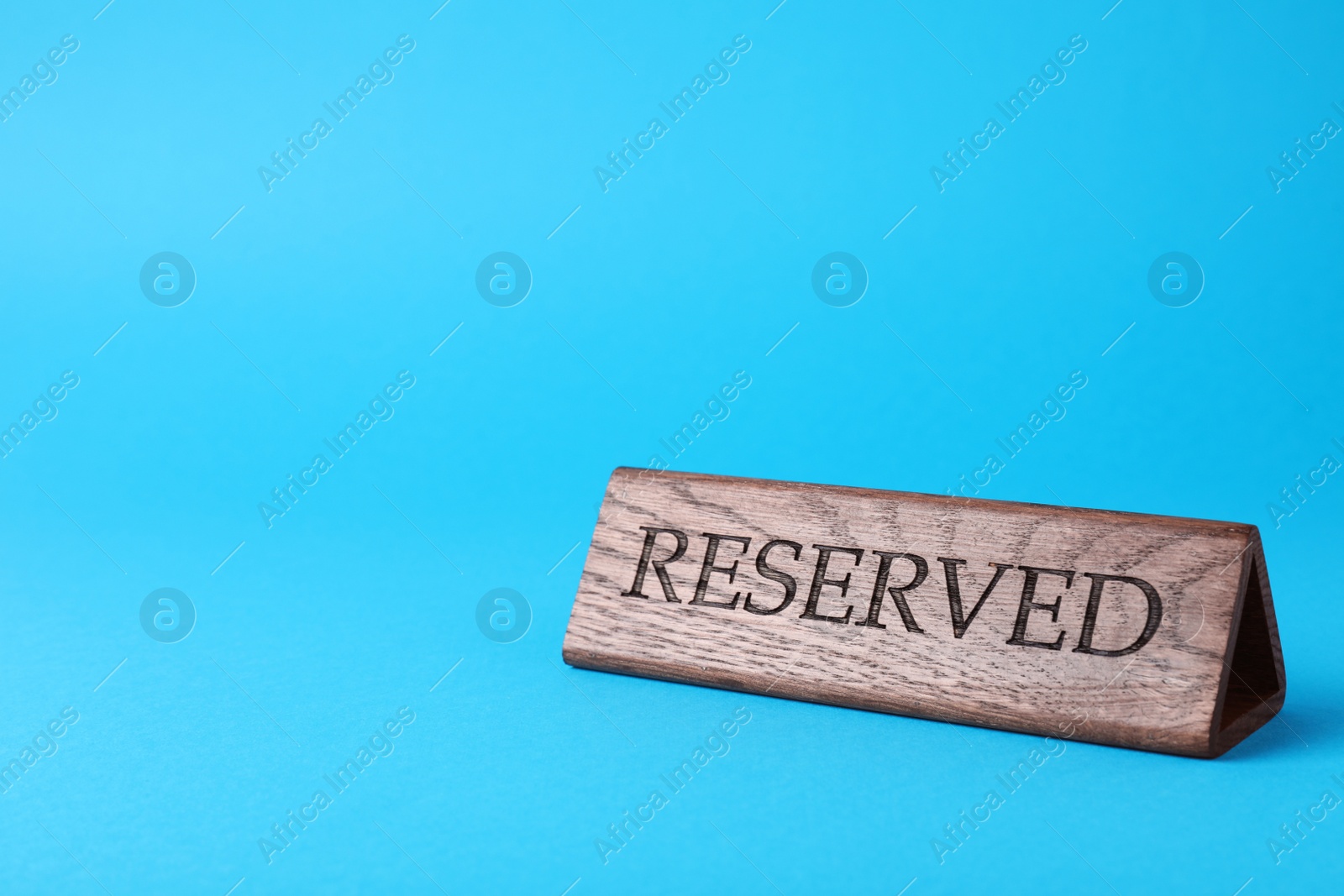 Photo of Elegant wooden sign Reserved on light blue background, space for text