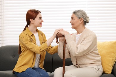 Photo of Caregiver and senior woman with walking cane sitting on sofa at home