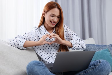 Photo of Woman making heart with hands during video chat via laptop at home. Long-distance relationship