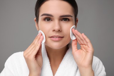 Photo of Young woman cleaning her face with cotton pads on grey background, closeup