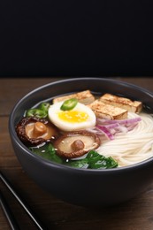 Delicious vegetarian ramen in bowl on wooden table against black background