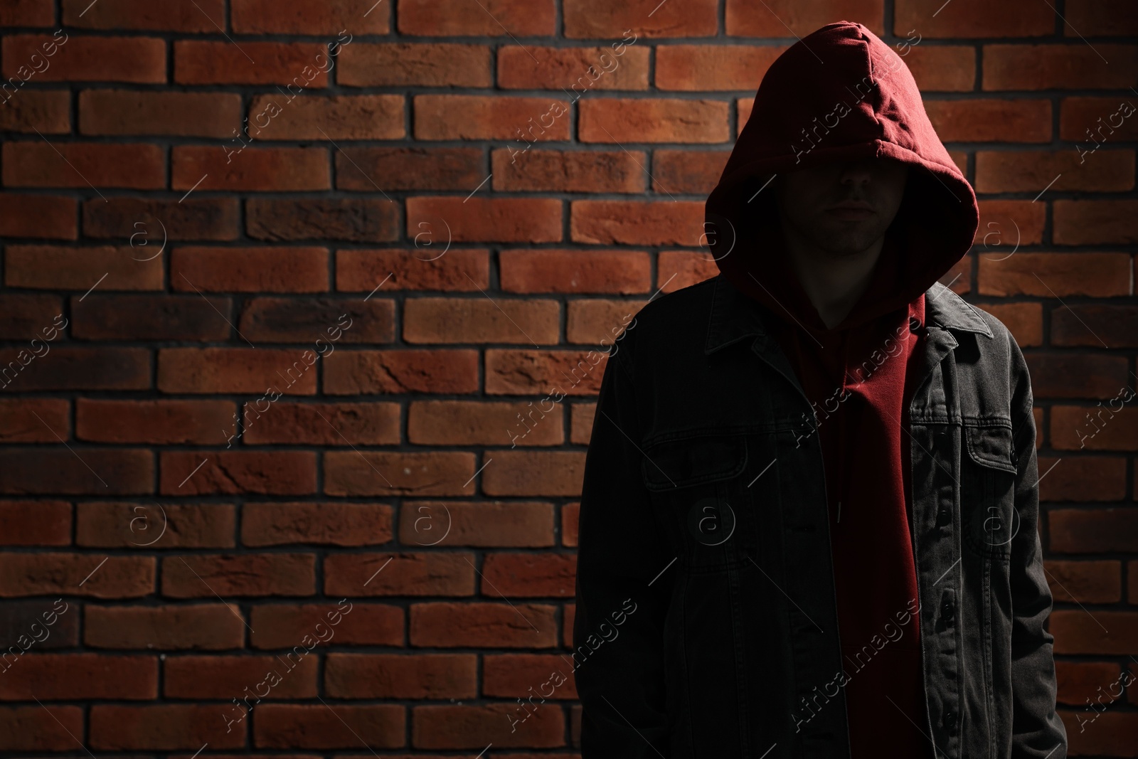 Photo of Thief in hoodie against red brick wall. Space for text