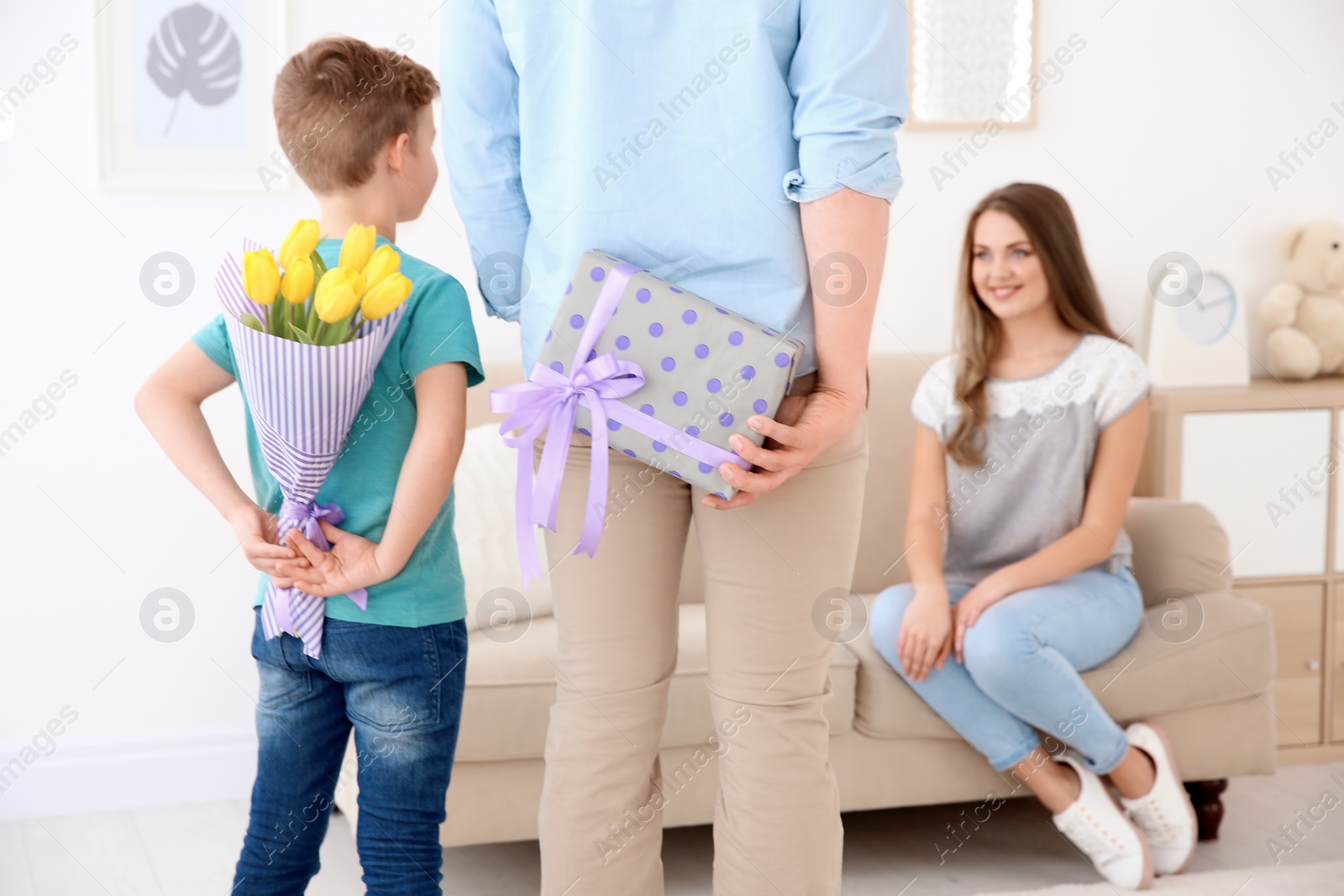 Photo of Husband and son hiding flowers and gift behind their backs at home