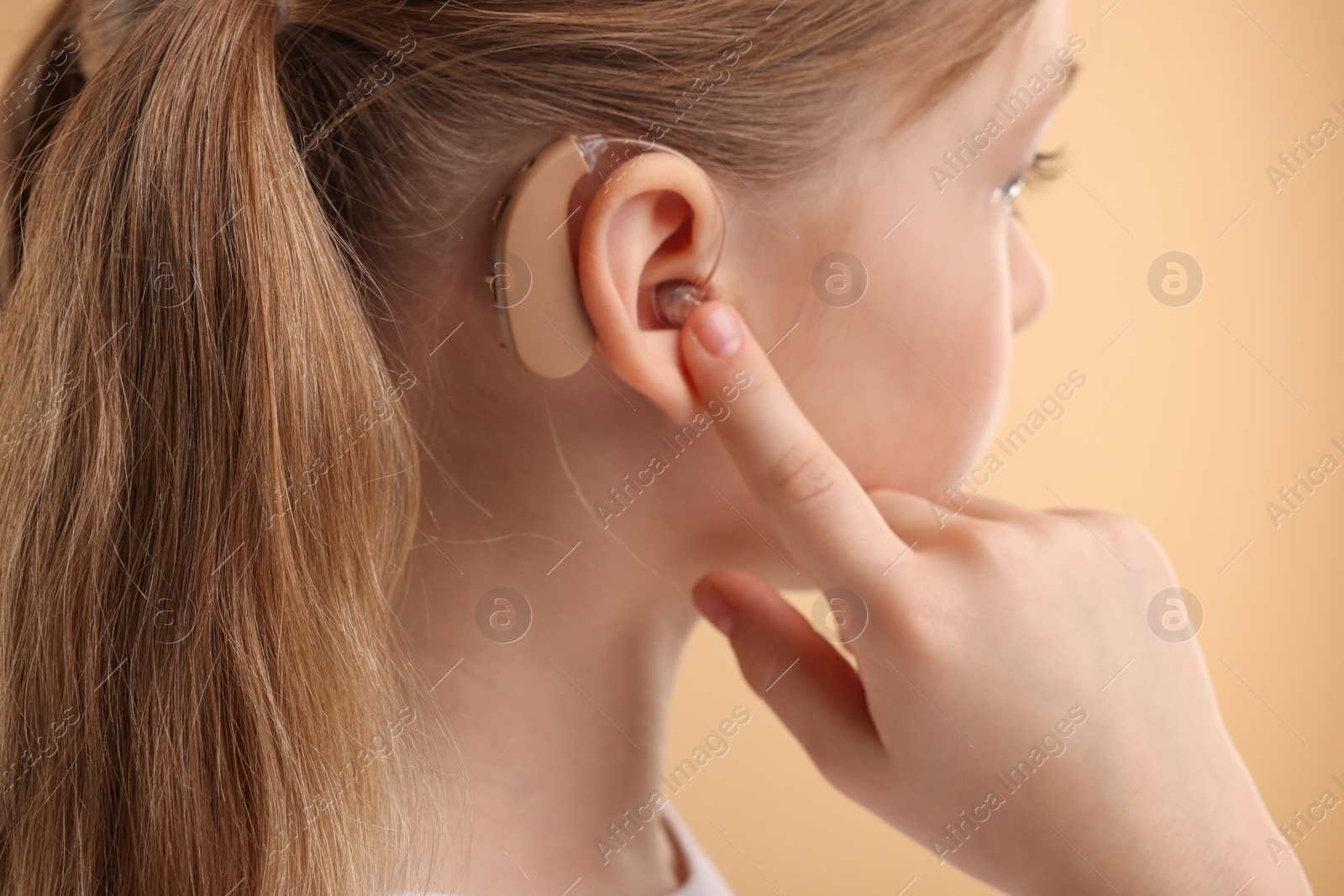 Photo of Little girl with hearing aid on pale brown background, closeup