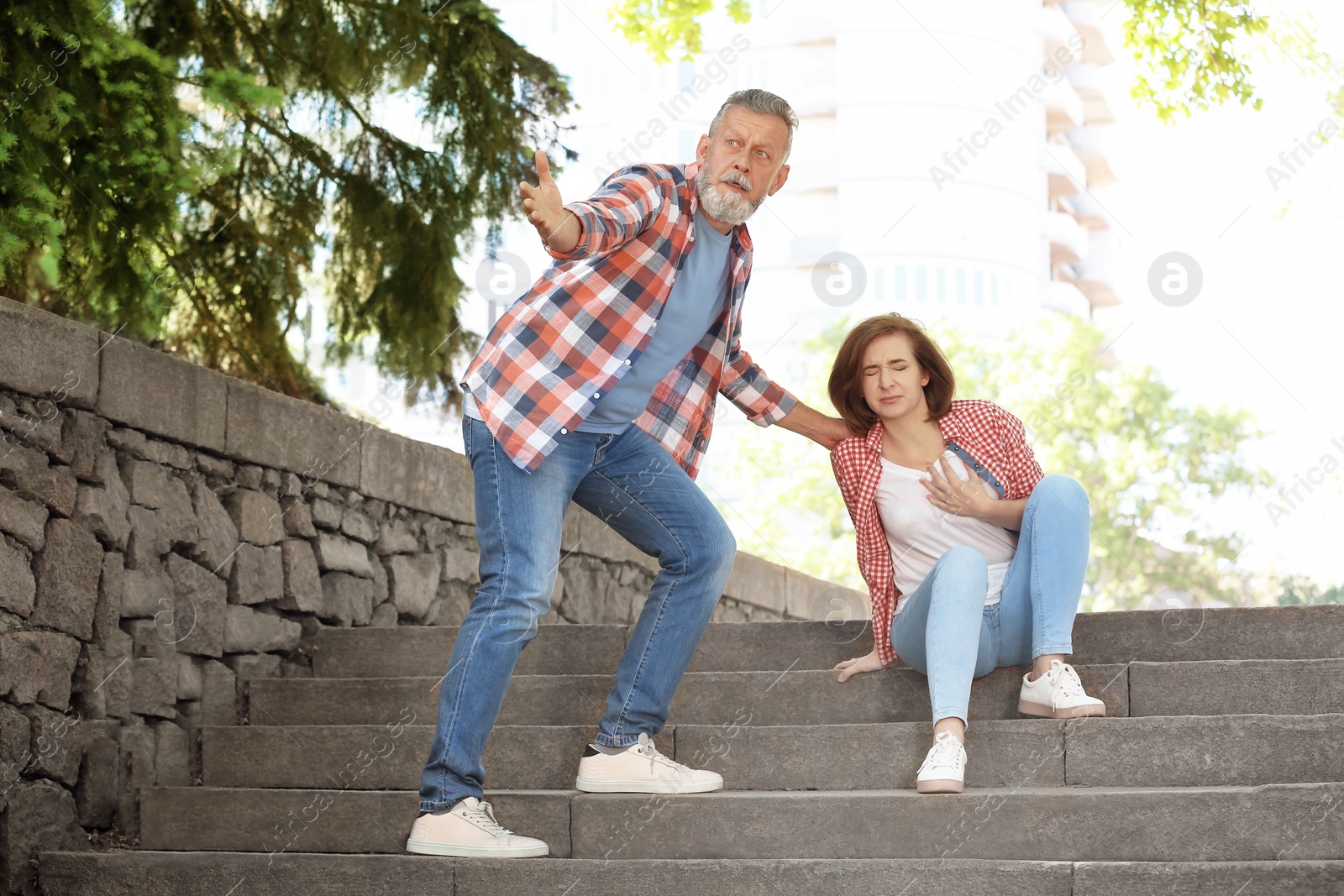 Photo of Man helping mature woman suffering from heart attack on stairs, outdoors