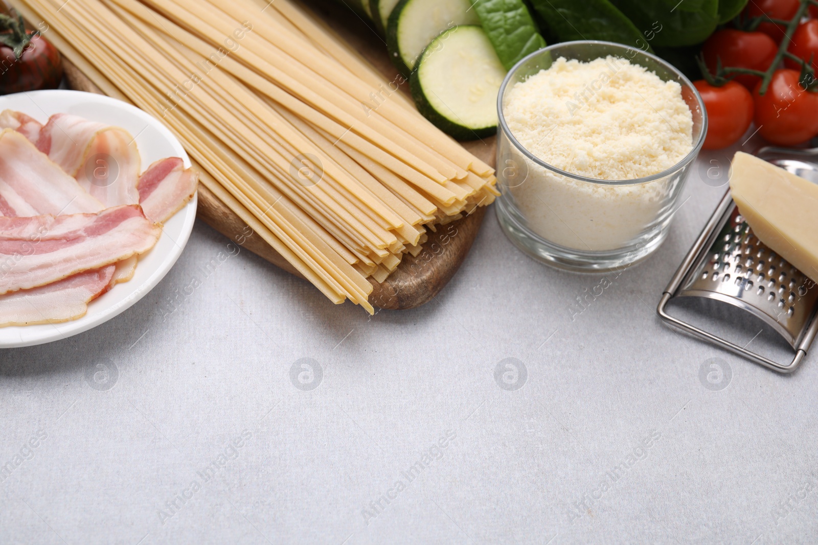 Photo of Raw pasta, bacon and fresh ingredients on light grey table, space for text