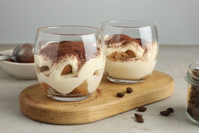 Photo of Delicious tiramisu in glasses and scattered coffee beans on light table