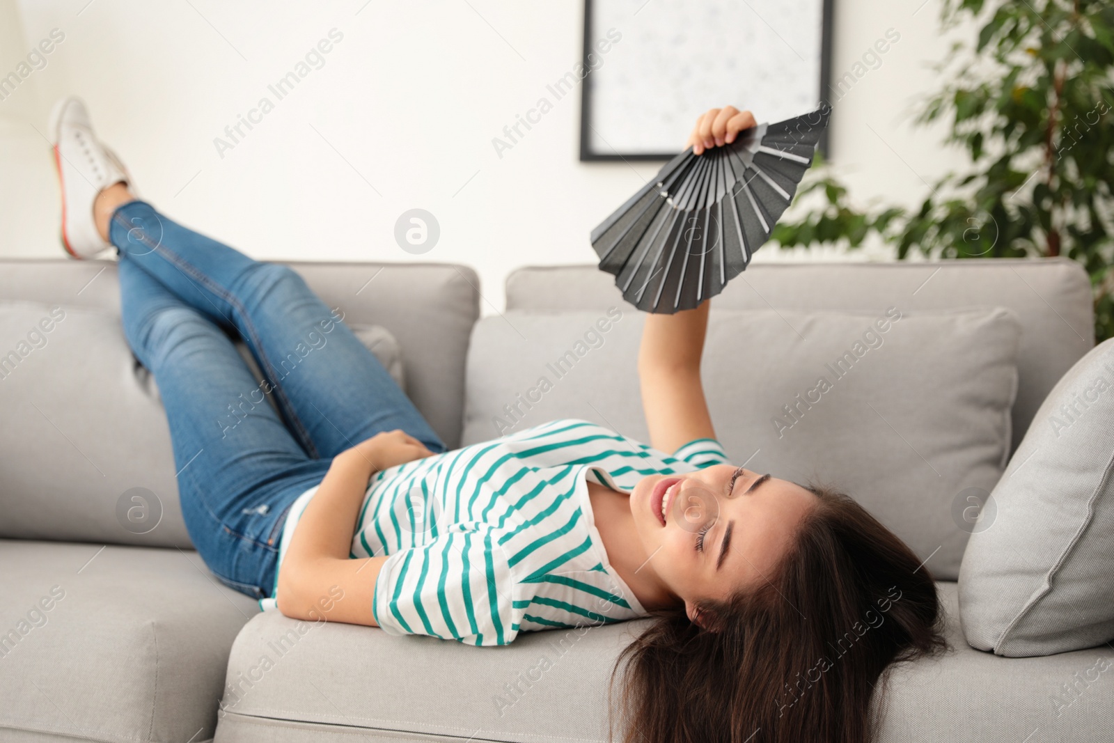 Photo of Woman enjoying air flow from hand fan at home. Summer heat