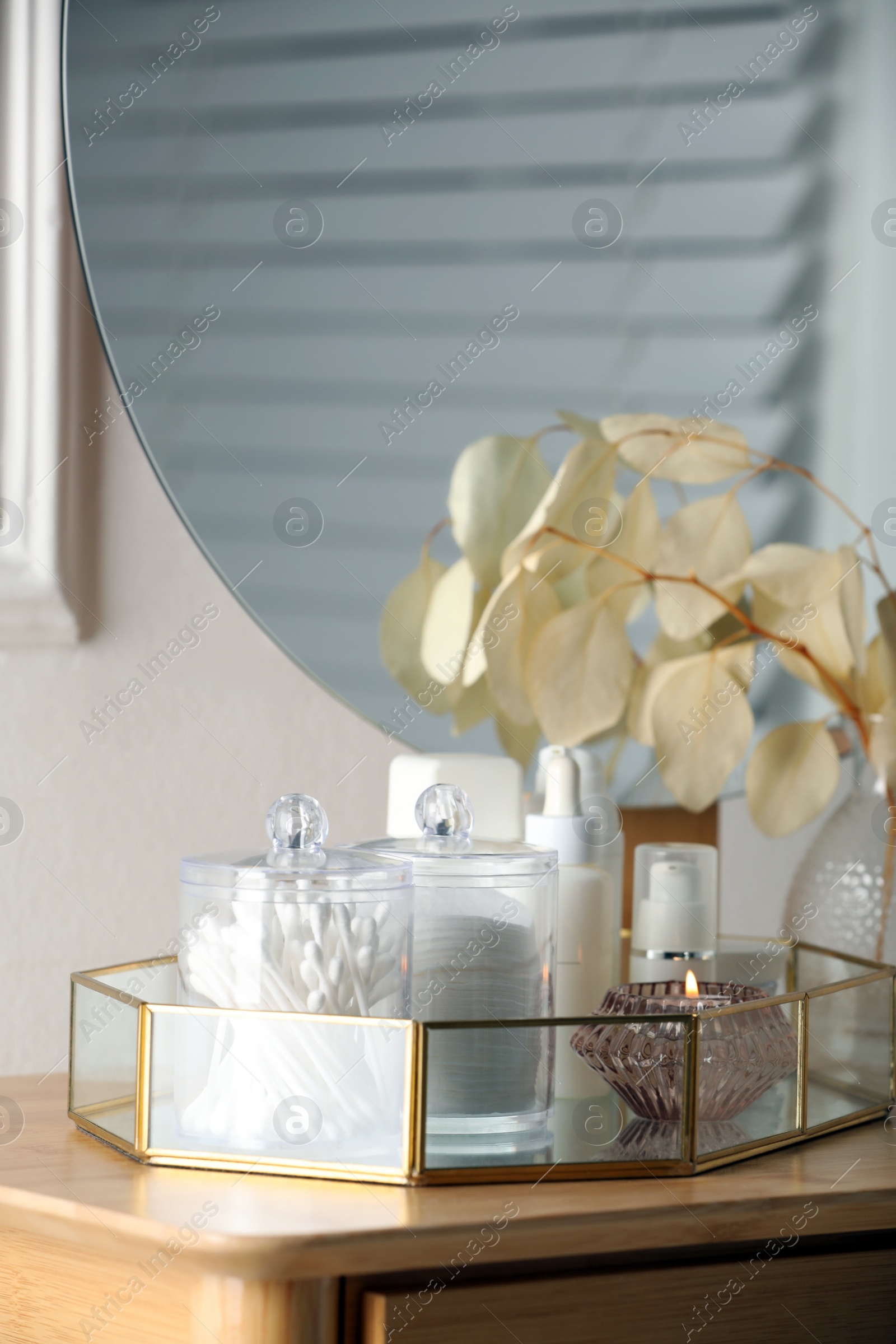Photo of Containers with cotton swabs, pads and burning candle near cosmetic products on dressing table