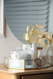 Containers with cotton swabs, pads and burning candle near cosmetic products on dressing table