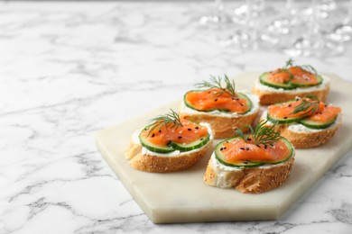Photo of Tasty canapes with salmon, cucumber and cream cheese on white marble table. Space for text