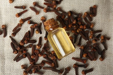 Photo of Essential oil and dried cloves on grey fabric, flat lay