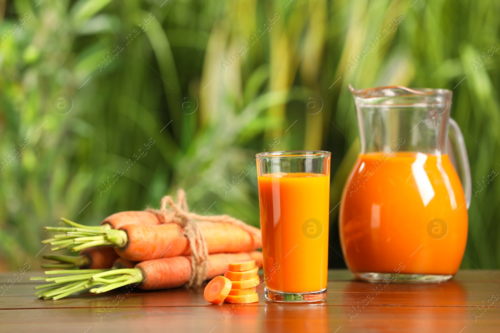 Photo of Tasty refreshing juice and fresh carrot on wooden table outdoors