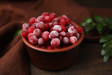 Frozen red cranberries in bowl on wooden table, closeup