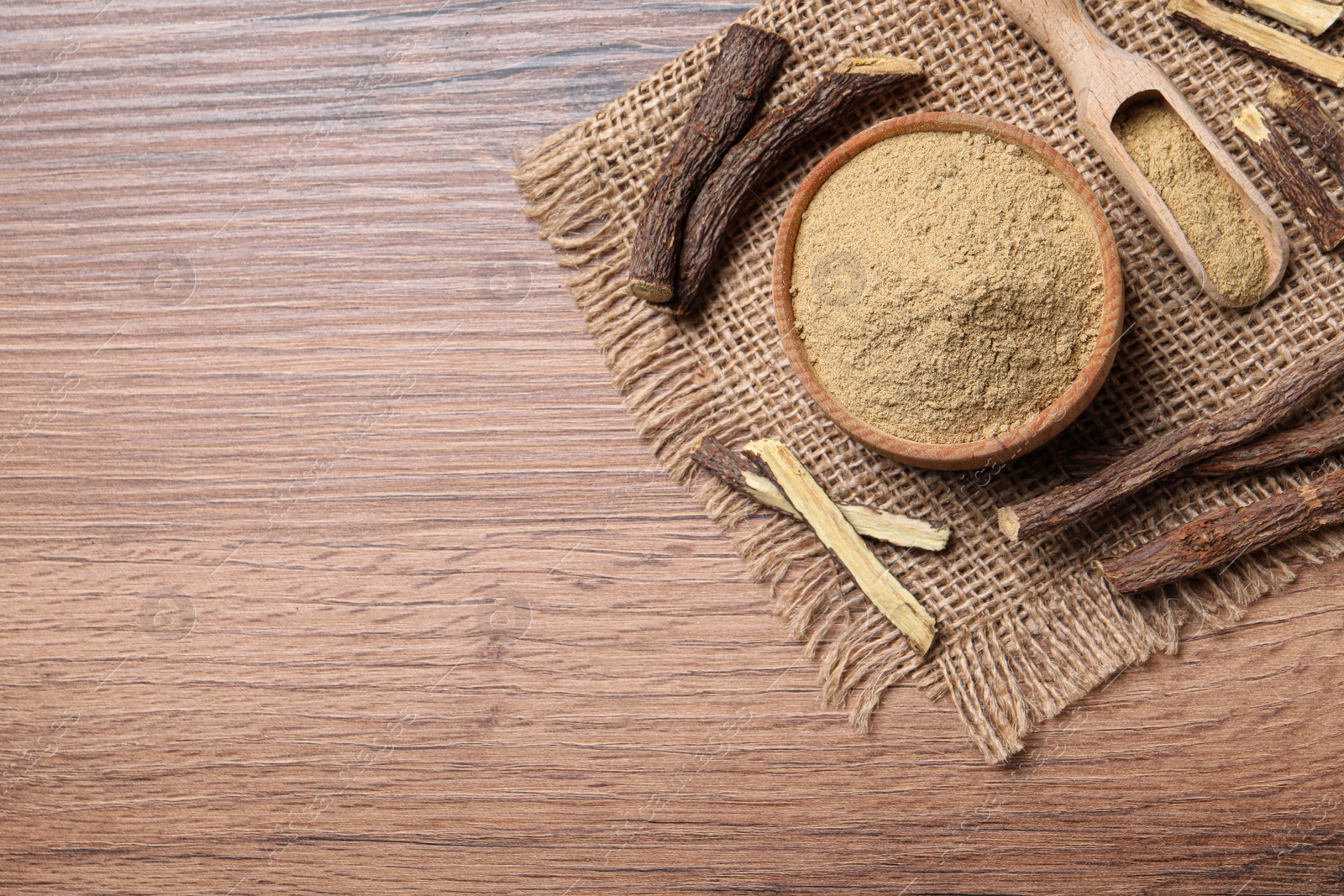 Photo of Dried sticks of liquorice root and powder on wooden table, flat lay. Space for text