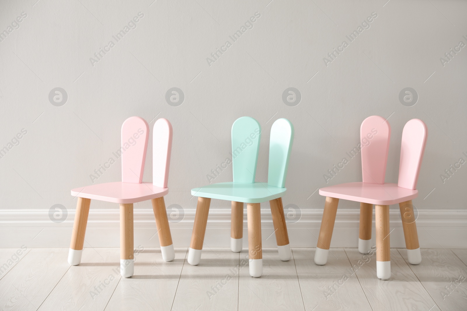 Photo of Cute little chairs with bunny ears near white wall indoors. Children's room interior