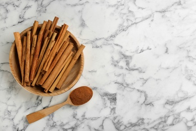 Photo of Aromatic cinnamon sticks and powder on white marble table, flat lay. Space for text