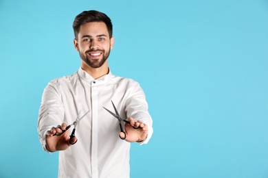 Young hairstylist holding professional scissors on color background, space for text