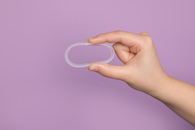 Photo of Woman holding diaphragm vaginal contraceptive ring on lilac background, closeup. Space for text