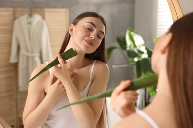 Photo of Young woman applying aloe gel from leaf onto her neck near mirror in bathroom