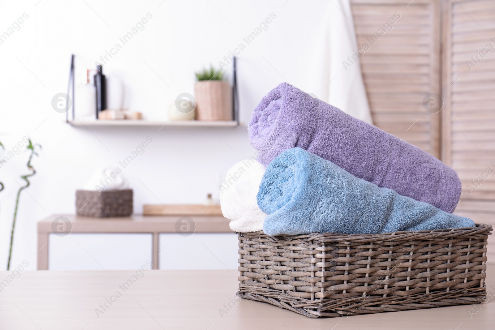 Photo of Basket with rolled fresh towels on table in bathroom. Space for text