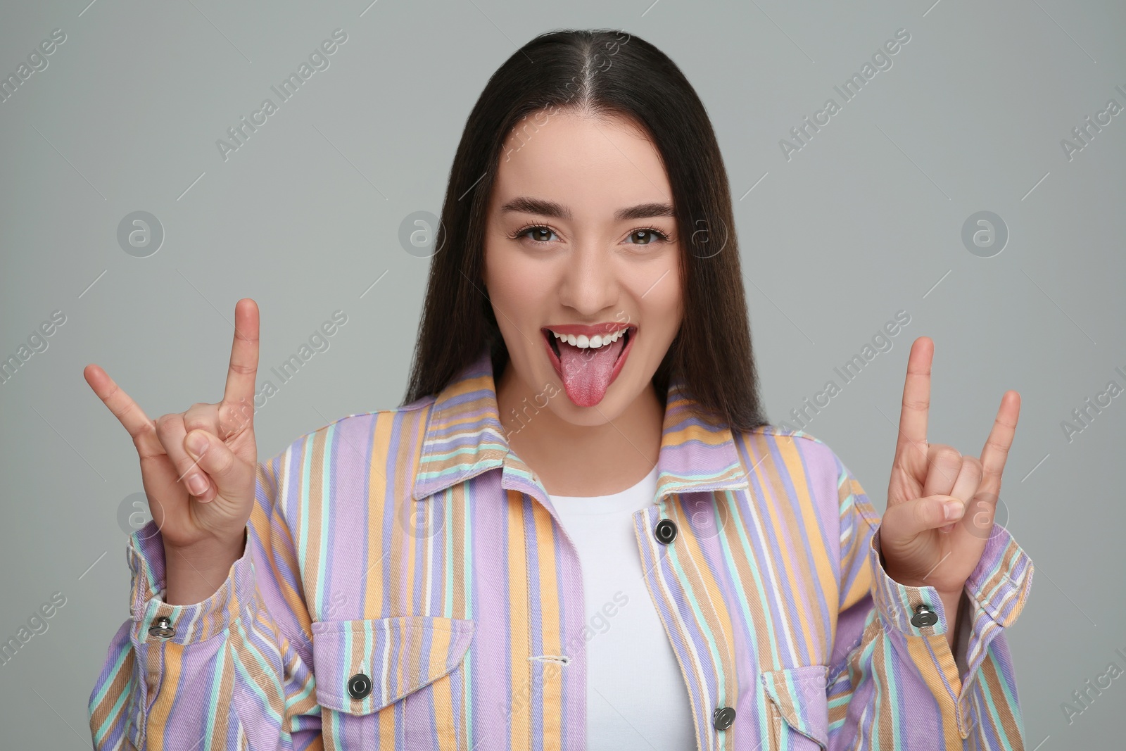 Photo of Happy woman showing her tongue and rock gesture on gray background