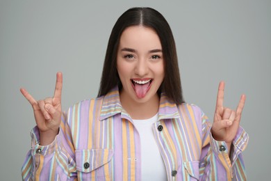 Photo of Happy woman showing her tongue and rock gesture on gray background