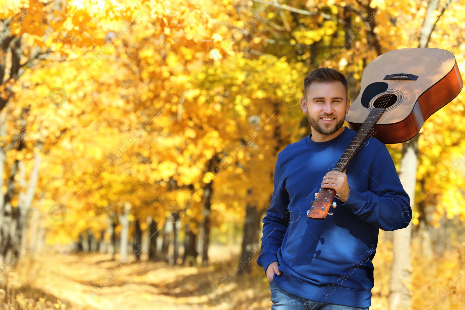 Photo of Young man with acoustic guitar in autumn park