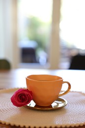 Photo of Cup of hot drink and red rose on table indoors