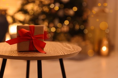 Photo of Beautiful gift box on wooden table in room decorated for Christmas. Bokeh effect