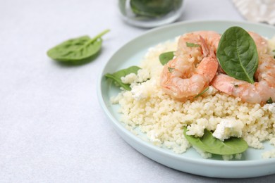 Photo of Plate of delicious couscous with shrimps and spinach on white table, closeup. Space for text