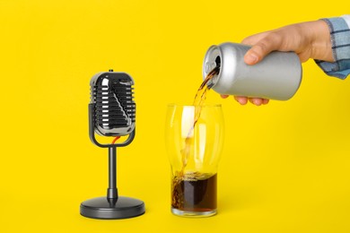 Woman making ASMR sounds with microphone and soda drink on yellow background, closeup