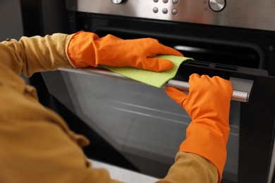 Photo of Woman with microfiber cloth cleaning electric oven in kitchen, closeup