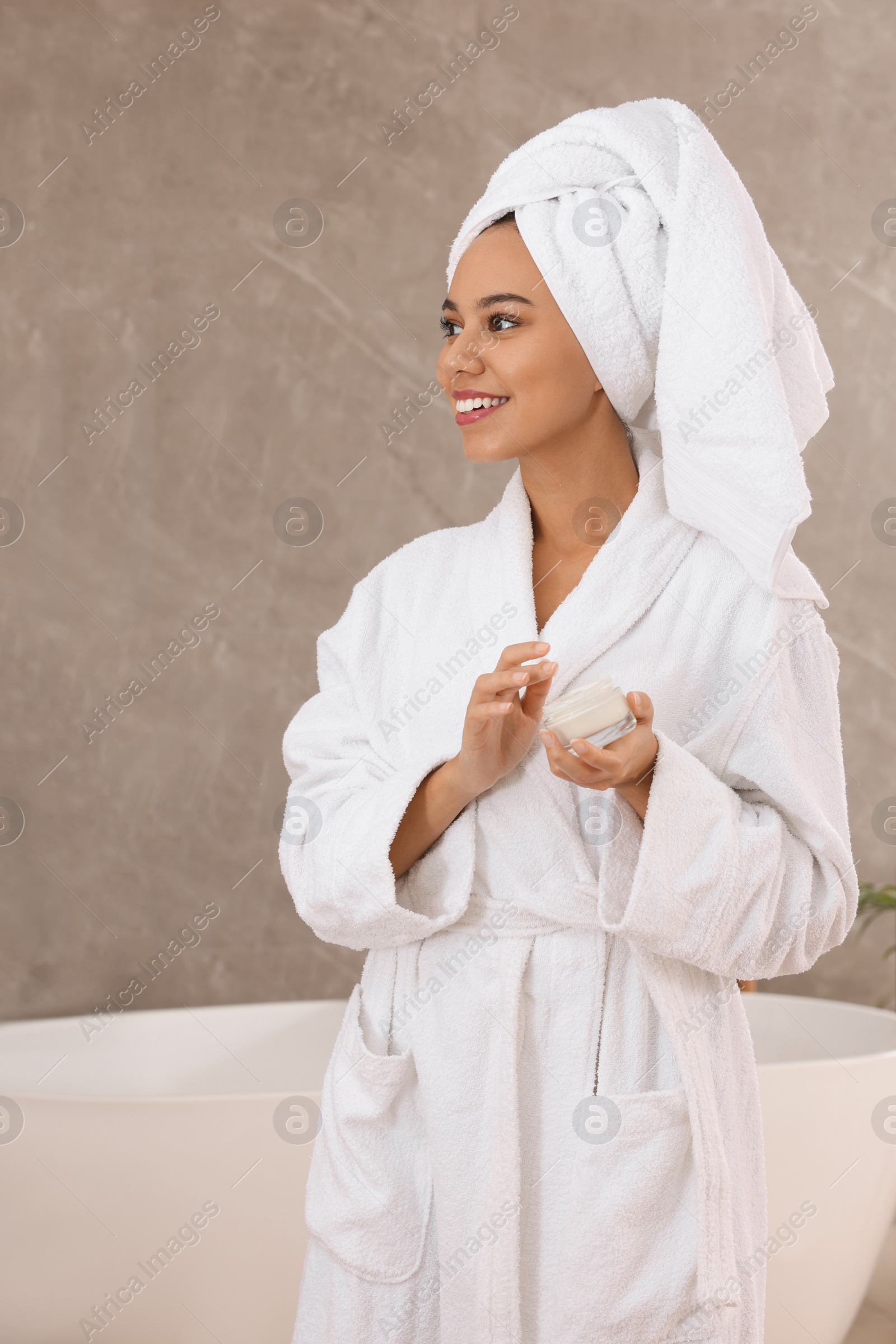 Photo of Beautiful African American woman with jar of cream in bathroom