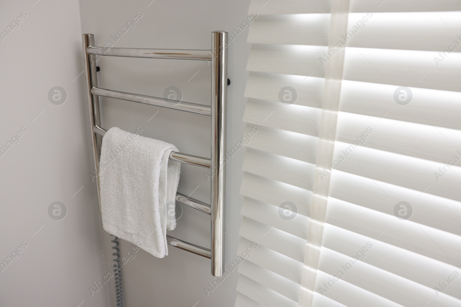 Photo of Heated rail with towel on white wall in bathroom, space for text