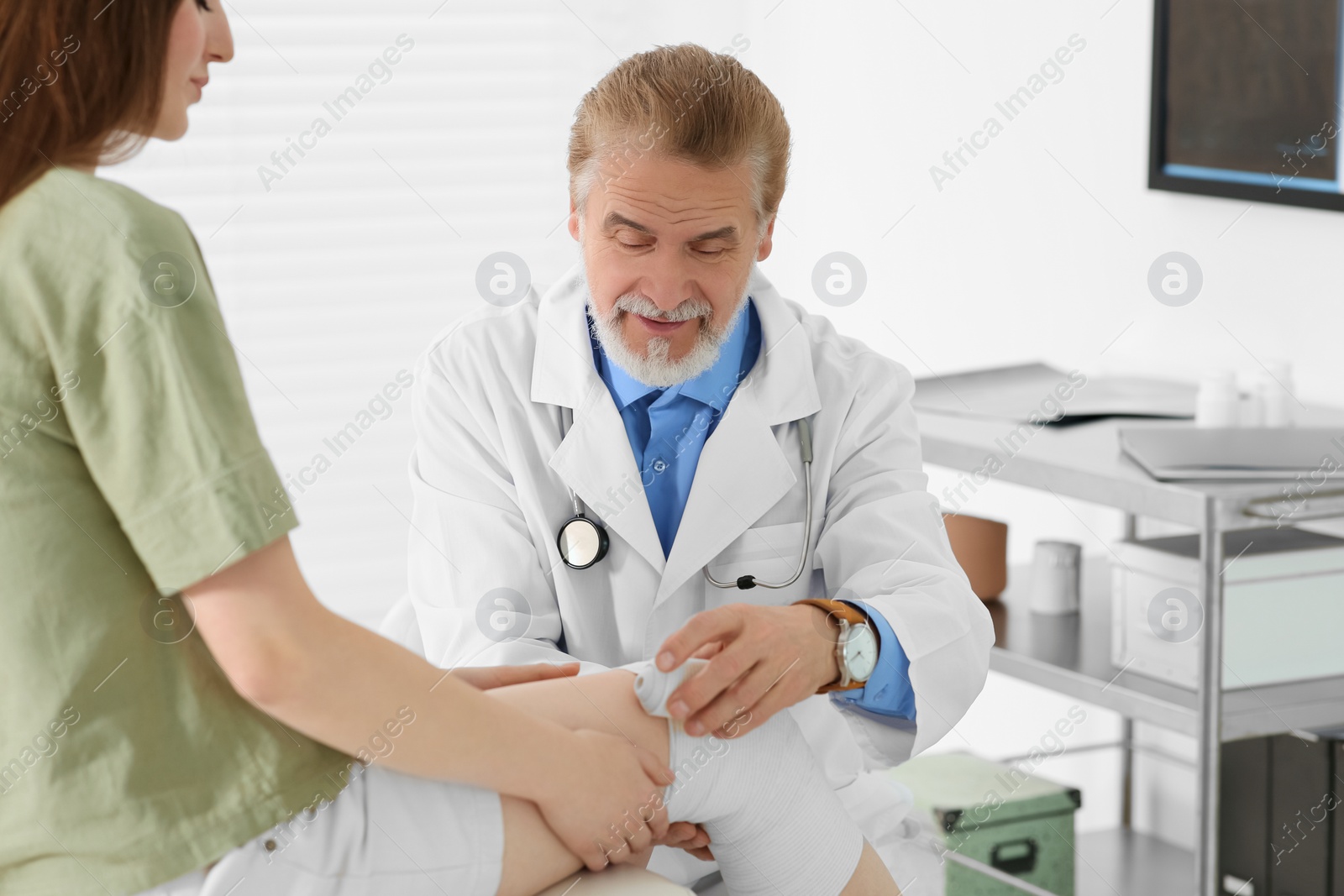 Photo of Orthopedist applying bandage onto patient's knee in clinic