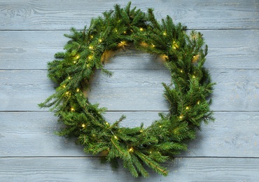 Photo of Beautiful Christmas wreath with festive lights on wooden background, top view