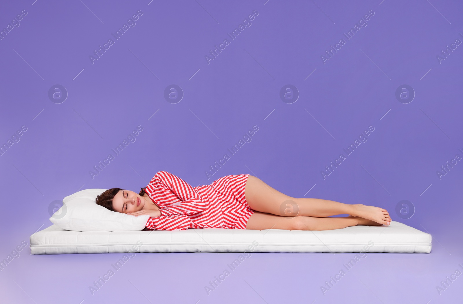 Photo of Young woman sleeping on soft mattress against light purple background