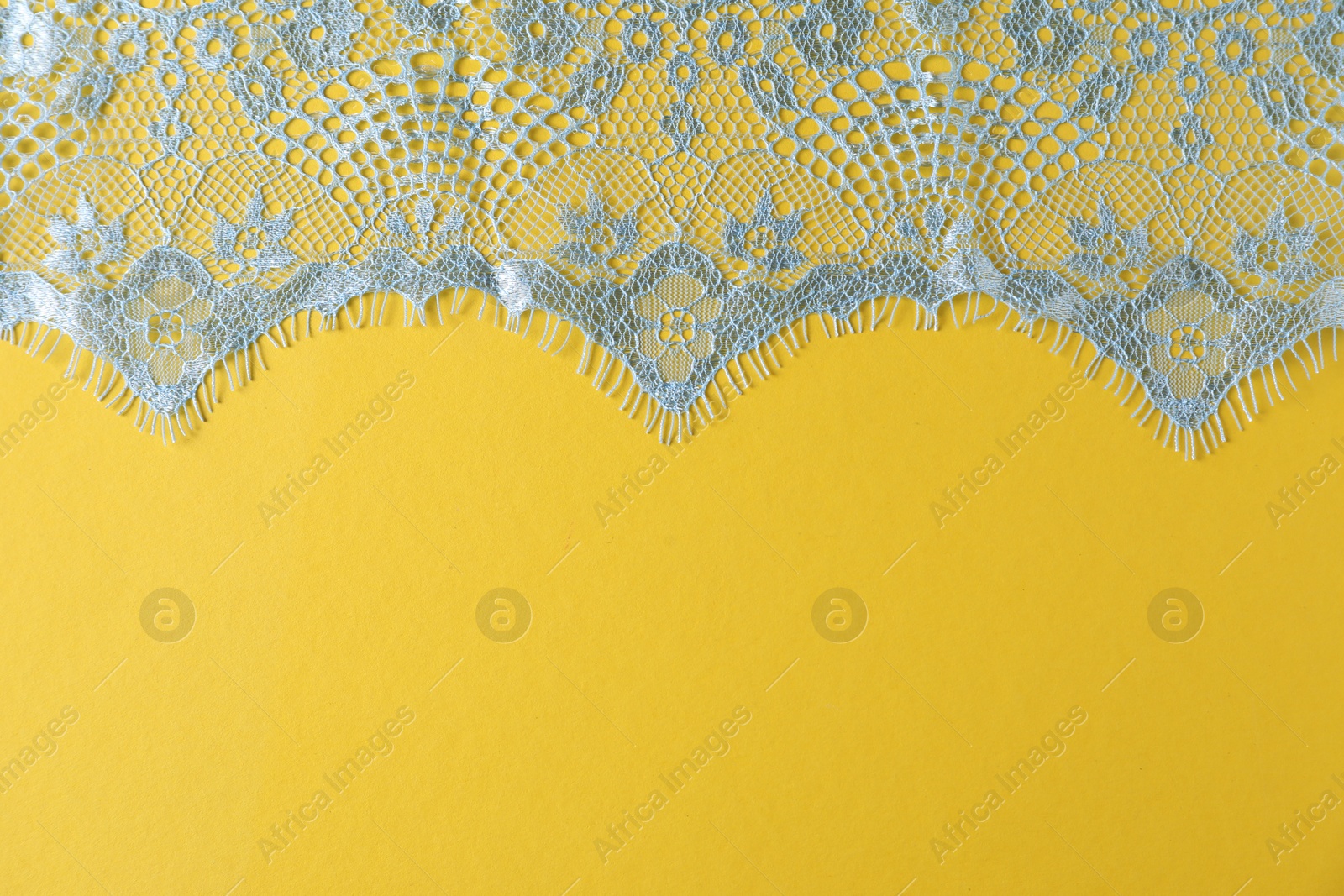 Photo of Light blue lace on yellow background, top view. Space for text