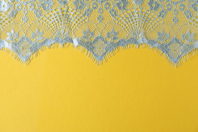 Photo of Light blue lace on yellow background, top view. Space for text