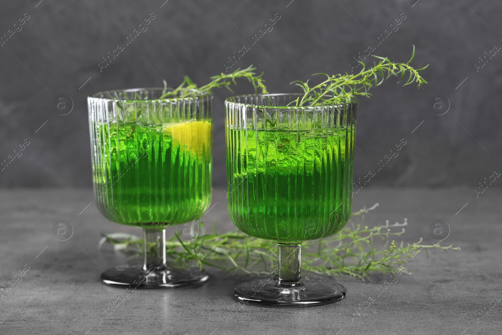 Photo of Glasses of homemade refreshing tarragon drink and sprigs on grey table