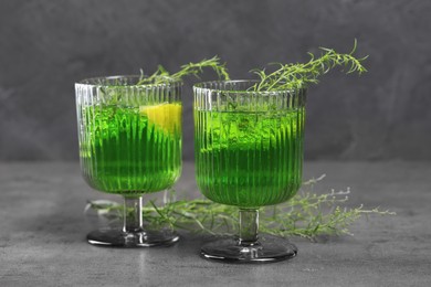 Photo of Glasses of homemade refreshing tarragon drink and sprigs on grey table