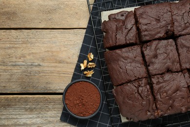 Delicious freshly baked brownies, cocoa powder and walnuts on wooden table, flat lay. Space for text