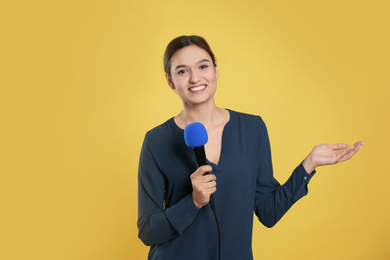 Young female journalist with microphone on yellow background