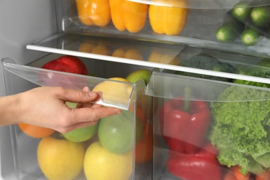 Photo of Woman opening refrigerator drawer with fresh fruits, closeup