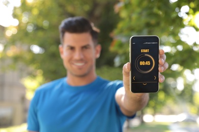 Photo of Man showing smartphone with fitness app outdoors, focus on device