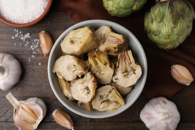 Photo of Pickled and fresh artichokes on wooden table, flat lay